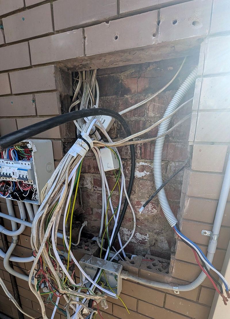 Old switchboard and loose cables on a brick wall before the upgrade