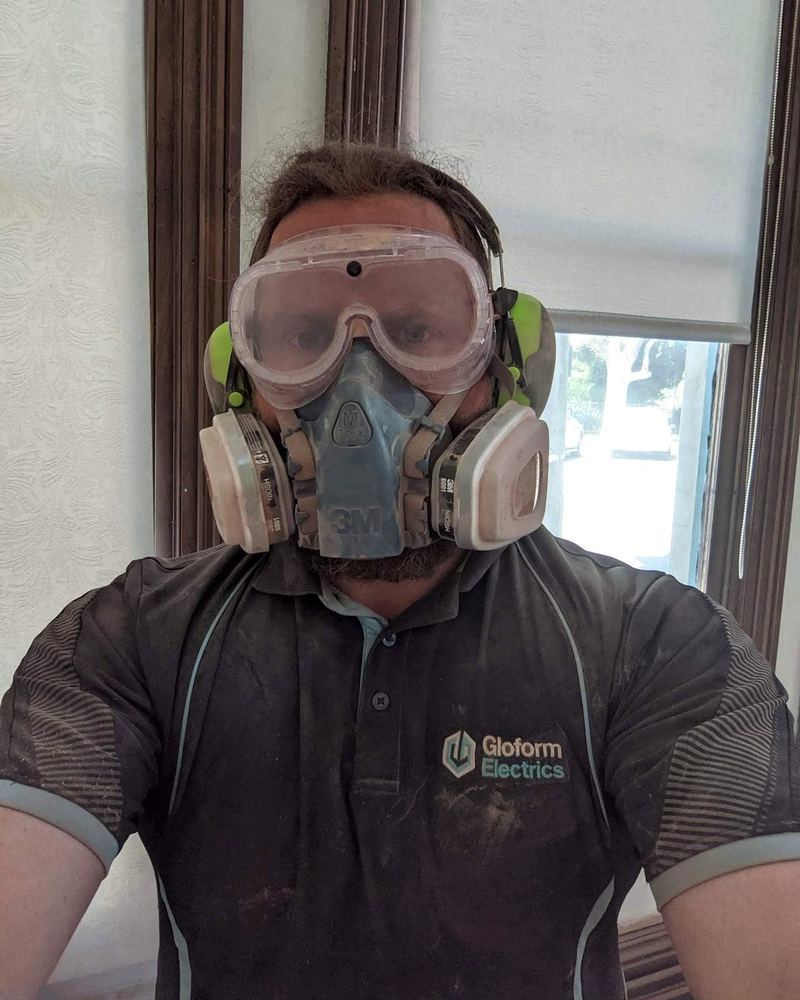 Gloform electrician in a dust mask, goggles, and earmuffs