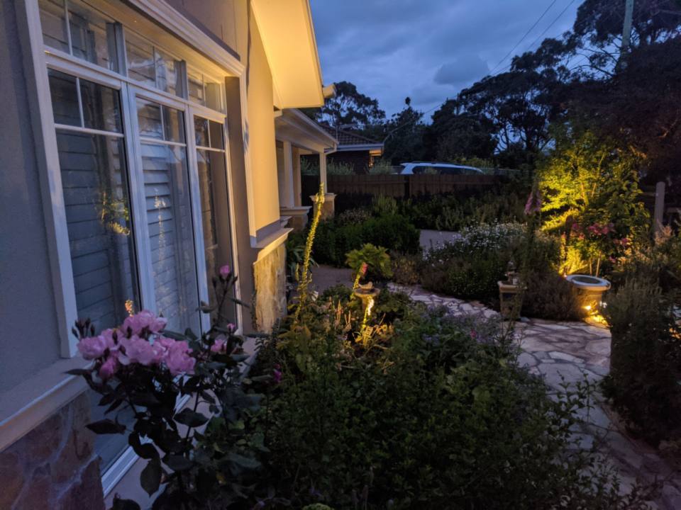 Garden beds and a stone path lit by warm spike lights beside a house in Mornington at dusk